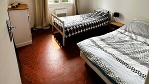 Une chambre avec deux lits, une petite armoire, un radiateur et une fenêtre avec des rideaux.