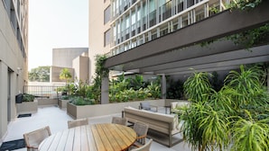Une terrasse extérieure avec une table ronde en bois et des chaises en osier, entourée de jardinières contenant différentes plantes.