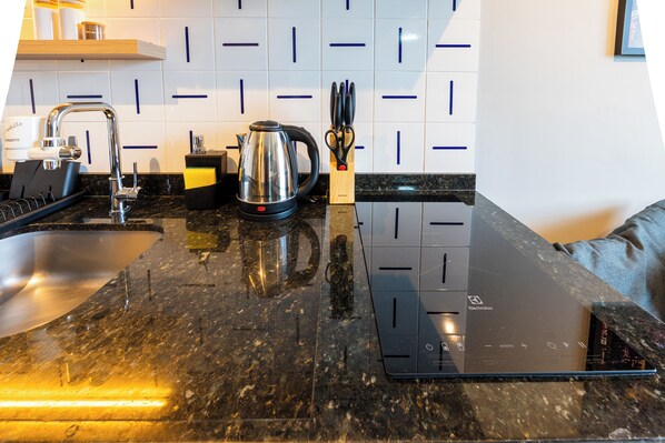 A modern kitchen with a black countertop, stainless steel kettle, and a built-in oven.