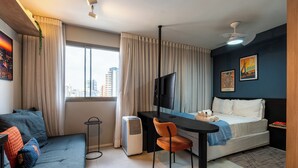 Une chambre d’hôtel moderne équipée d’un lit, d’un bureau, d’une chaise, d’une télévision et d’une grande fenêtre avec des rideaux.