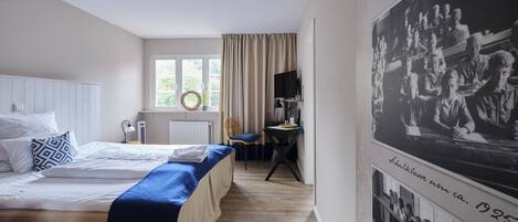 A bedroom with a bed, a desk, a chair, a window, and a wall with black and white photos.
