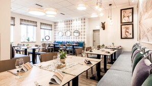 A restaurant with multiple tables and booths, some with plants and menus. - Hotel Utspann - Schafflund (Schafflund)
