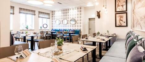 Un restaurant doté de nombreuses tables et de plusieurs coins salons, dont certains sont agrémentés de plantes et de menus.