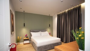 A modern bedroom with a large bed, bedside tables, a wooden nightstand, a potted plant, and a red sign on the door. - Villa Klaus Center Hotel  (Tirana)
