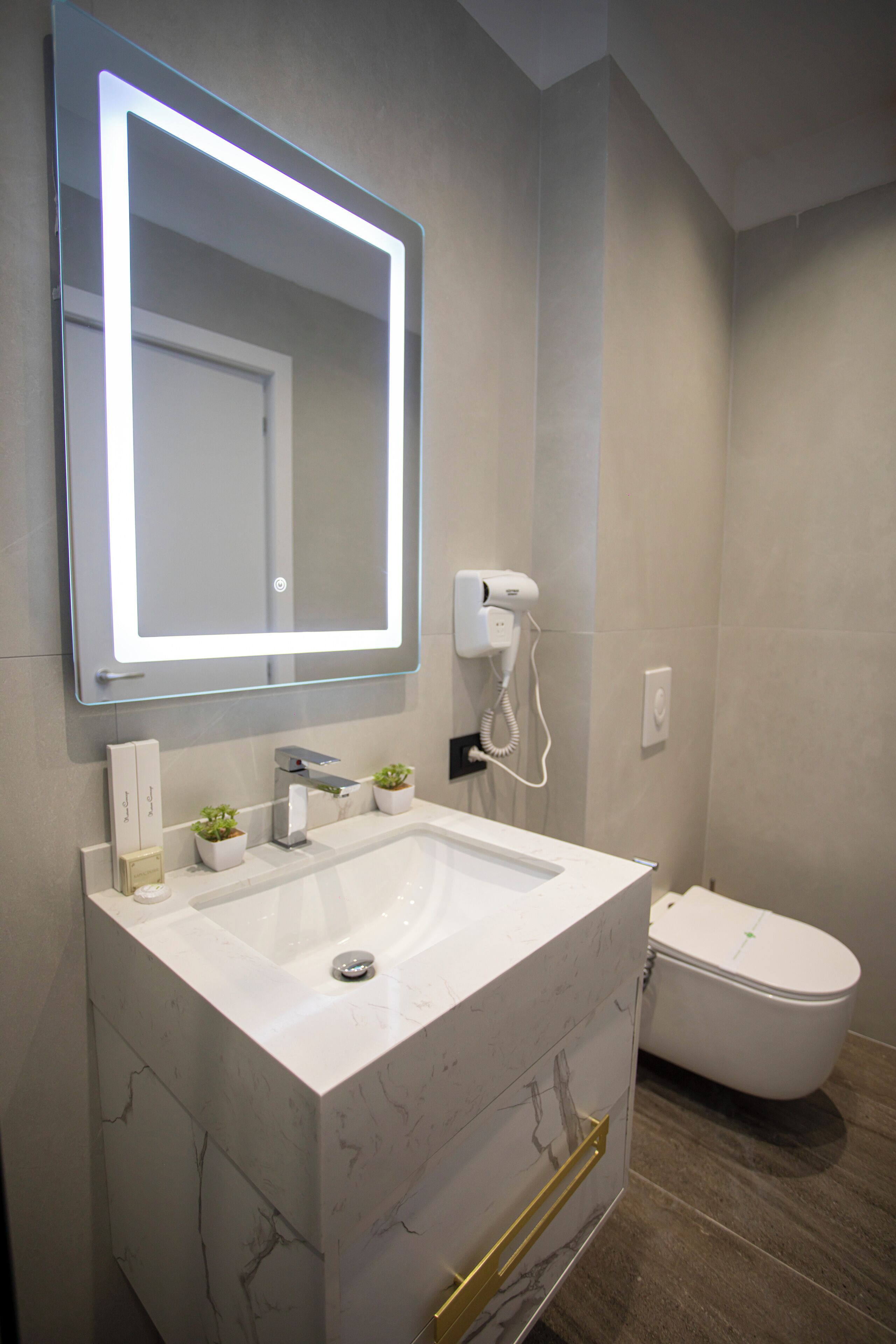Ein Badezimmer mit einem weißen Waschbecken, einem Spiegel mit LED-Beleuchtung, einem Föhn und einer Toilette.