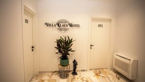 A hallway with doors labeled 101 and 102, a sign for Villa Klaus Hotel, a potted plant, a small statue, and a radiator. - Villa Klaus Center Hotel  (Tirana)