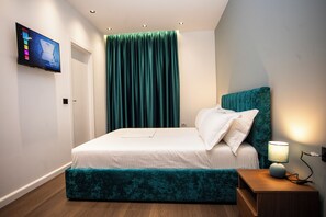 Un dormitori modern amb un llit, una tauleta de nit, un televisor fixat a la paret i una finestra amb cortines.