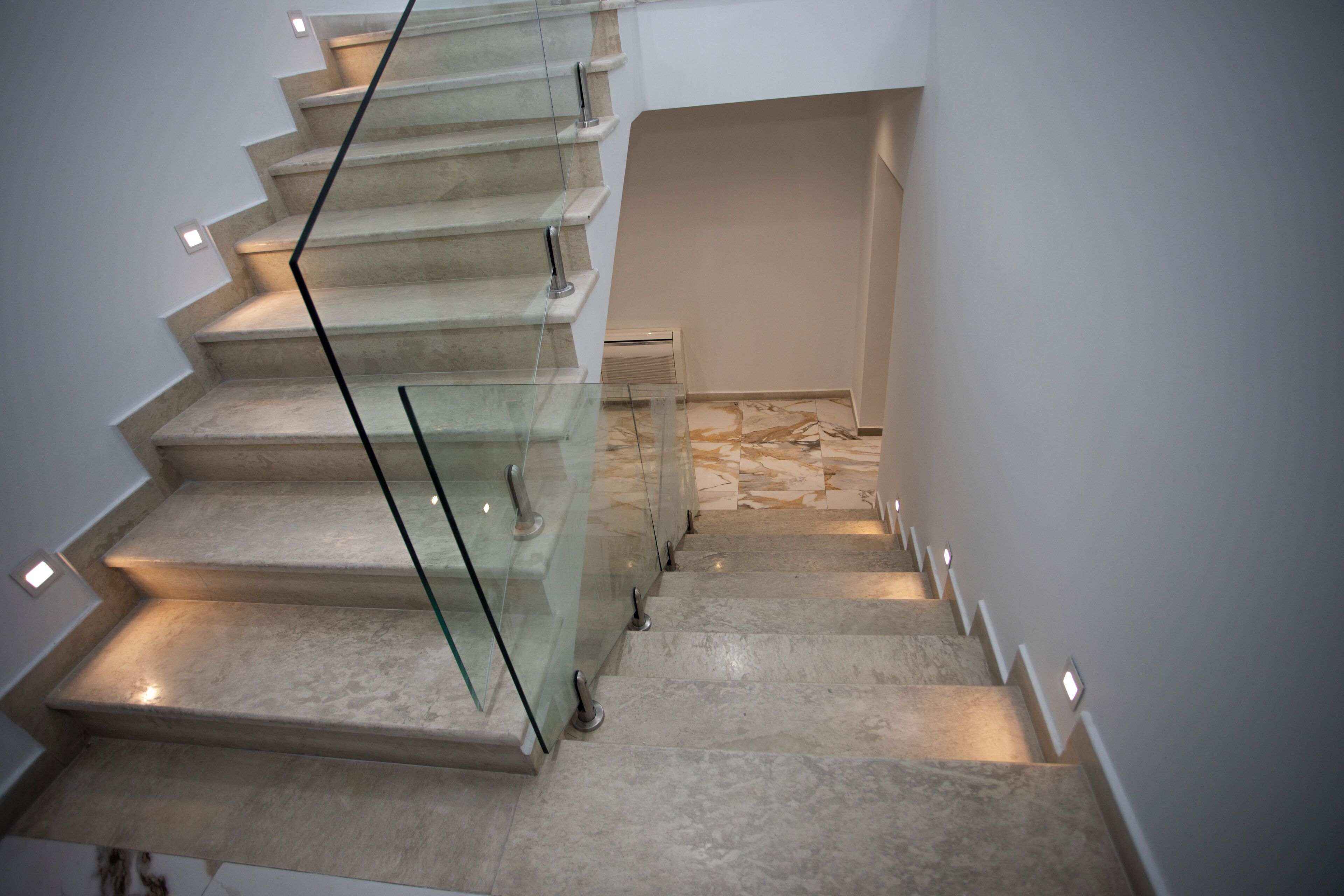 A modern staircase with glass railings and built-in lighting, leading to a landing area with a patterned floor.