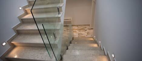 A modern staircase with glass railings and built-in lighting, leading to a landing area with a patterned floor.