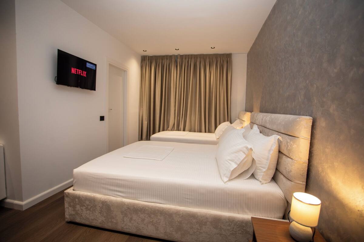 Moderni hotellihuone, jossa on suuri sänky, seinälle asennettu taulutelevisio ja yöpöytä, jossa on lamppu.