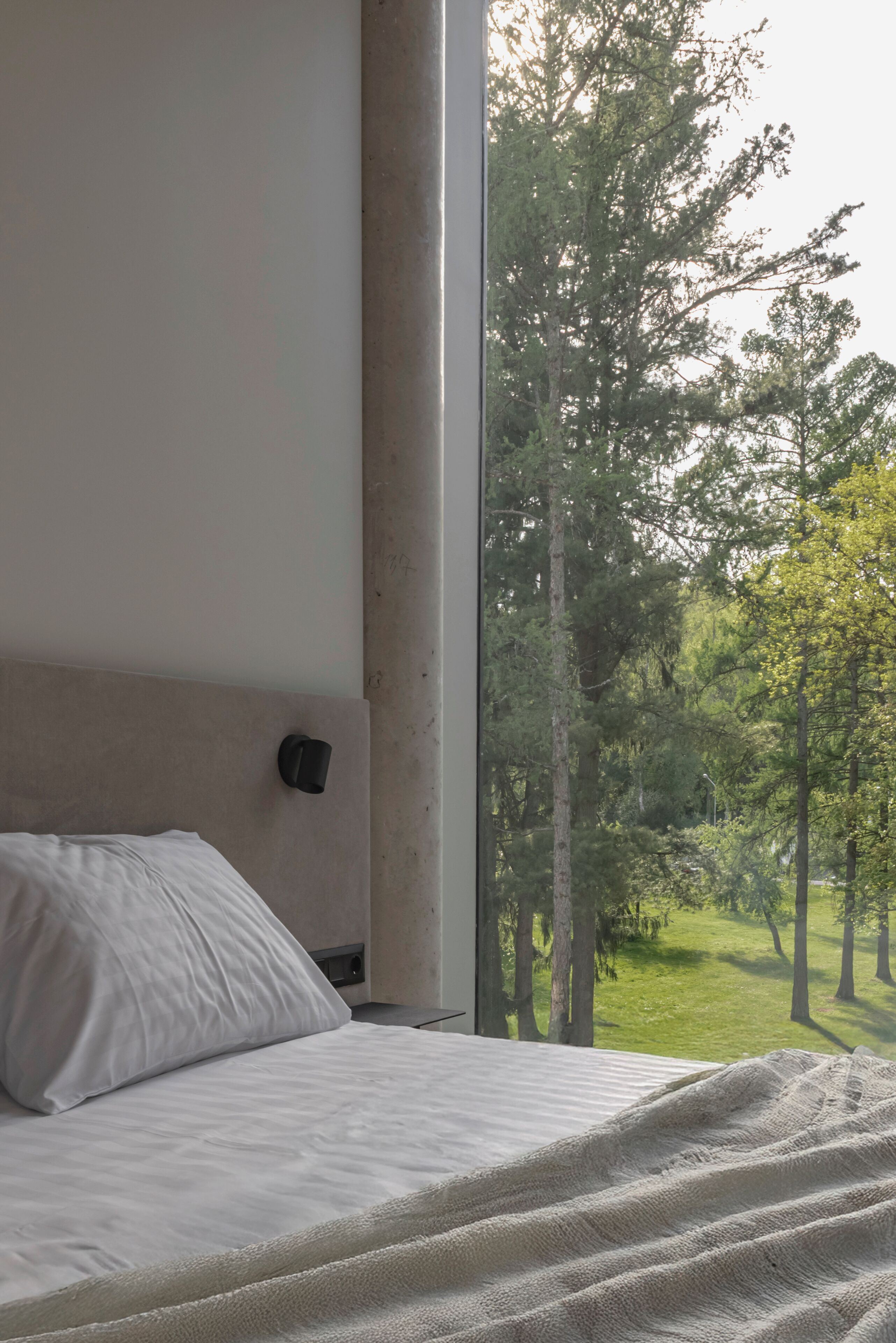 A bedroom with a large window, a bed, and a nightstand.