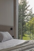 A bedroom with a large window, a bed, and a nightstand.