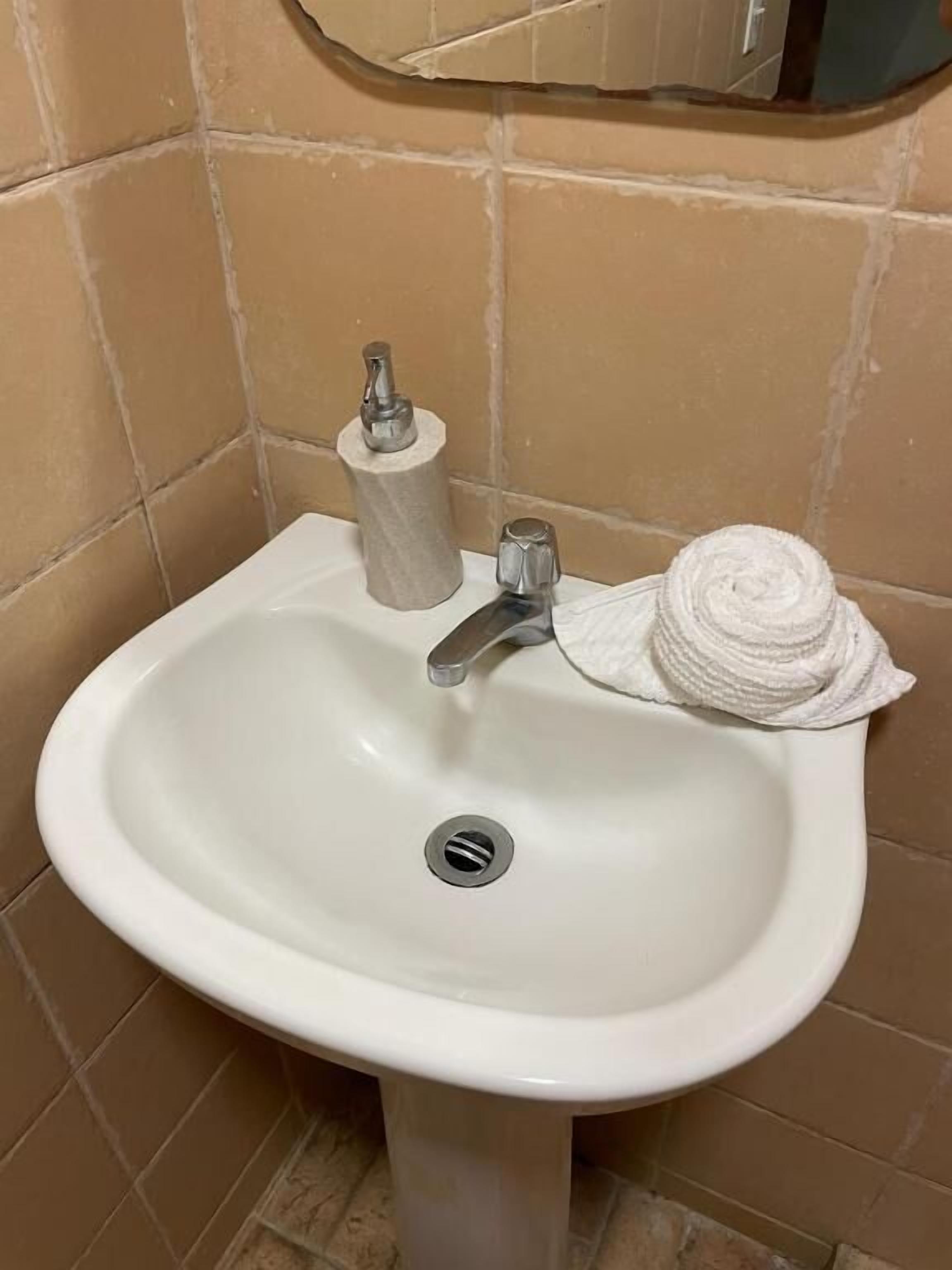 Un lavabo blanc dans une salle de bain, avec un robinet argenté, un porte-serviettes en papier et une serviette enroulée.