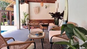 A covered outdoor seating area with wicker furniture, hanging lights, and potted plants.