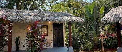 A small, single-story structure with a thatched roof, surrounded by lush greenery and a well-maintained lawn.