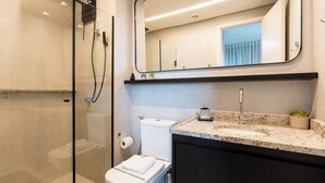 Un baño moderno con ducha de vidrio, inodoro, lavamanos con encimera de granito y espejo sobre el lavamanos.