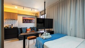 Una habitación de hotel moderna con una cama, un escritorio, un sofá, un televisor y una pintura de un paisaje urbano.