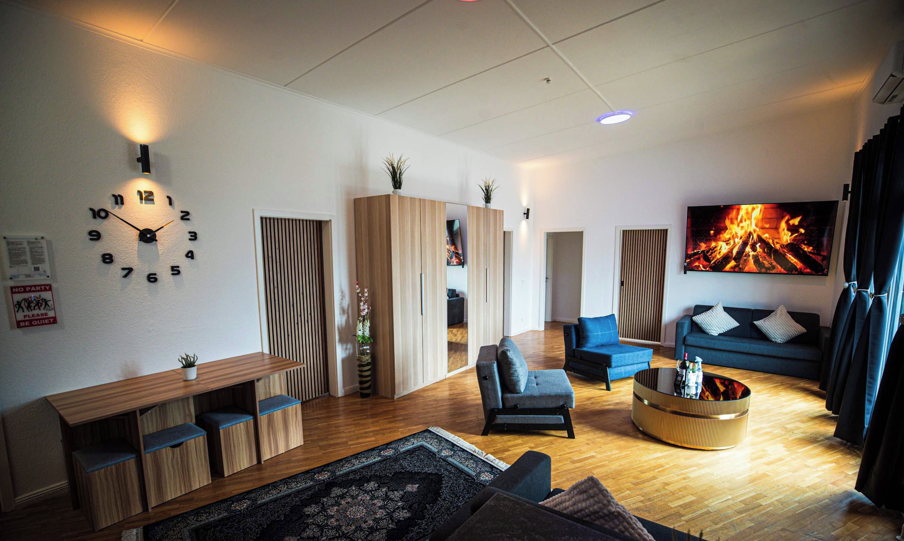 Ein modernes Wohnzimmer mit Holzboden, einem blauen Sofa, einem Couchtisch und einer Wanduhr.