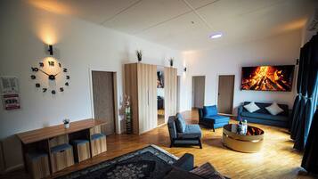 Ein modernes Wohnzimmer mit Holzboden, einem blauen Sofa, einem Couchtisch und einer Wanduhr.