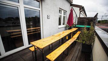 Eine Terrasse mit Holztischen und -bänken, einem roten Sonnenschirm und einem Blumentopf.