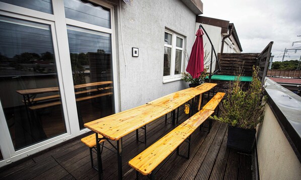 A terrace with wooden tables and benches, a red umbrella, and a potted plant.