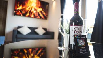 A bottle of wine, a glass, and a QR code on a table with a view of a room featuring a fireplace and a sofa.