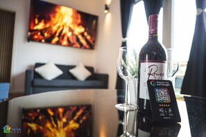 A bottle of wine, a glass, and a QR code on a table with a view of a room featuring a fireplace and a sofa.
