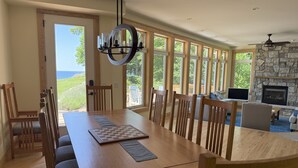 A dining area with a wooden table and chairs, a chandelier, and a stone fireplace. - Five bedroom home overlooking Lake MI, North of Leland. (Leland)