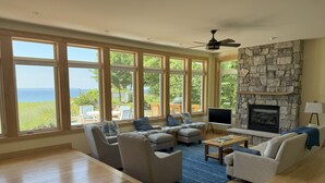 A spacious living room with large windows, a stone fireplace, and a view of the ocean. - Five bedroom home overlooking Lake MI, North of Leland. (Leland)