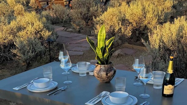 A table set for two with a bottle of Grütter wine, glasses, and a potted plant, overlooking a mountainous landscape.