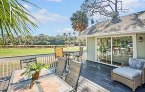 A deck with outdoor furniture, a glass door leading to a patio, and a view of a golf course.