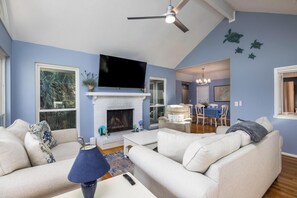 A living room with a fireplace, a television, and a dining area with a chandelier.