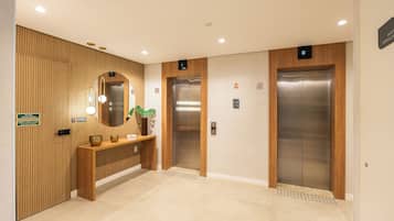 A modern elevator lobby with wooden paneling, a reception desk, and two elevators.