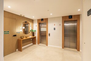 Un hall d’ascenseur moderne avec des panneaux de bois, un comptoir d’accueil et deux ascenseurs.