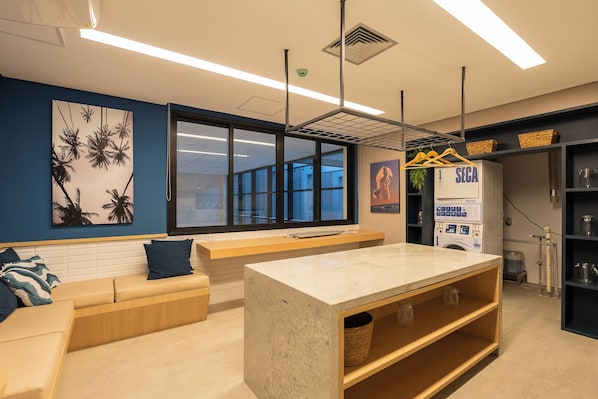 A modern kitchen with a central island, a seating area with a sofa and a bench, and a wall-mounted drying rack. - Viva Benx Pompéia (São Paulo)