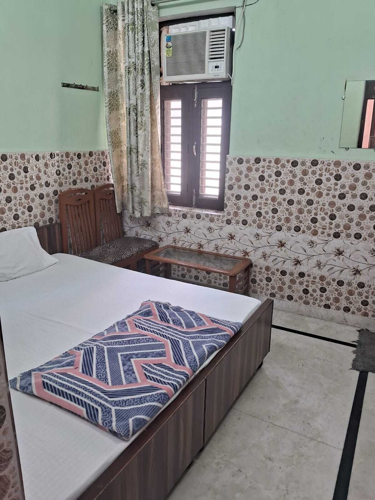 A bedroom with a bed, a wooden bench, a window with curtains, and a wall with a circular pattern.