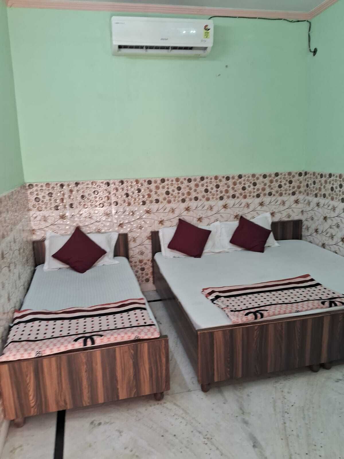 A room with two wooden beds, each with a patterned bedspread and pillows. An air conditioner is mounted on the wall above the beds.