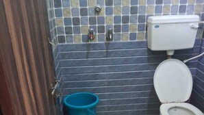 Ein kleines Badezimmer mit Toilette, einem blauen Mülleimer und einer gefliesten Wand.