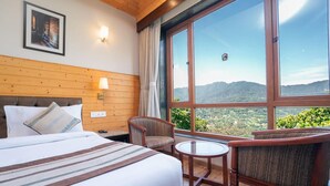 A hotel room with a large bed, two chairs, a small table, and a large window offering a mountain view. - Voyage Alpine Abode (Gangtok)