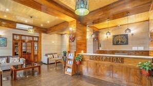 A reception area with a wooden reception desk, a sofa, a coffee table, and a plant. - Voyage Alpine Abode (Gangtok)