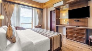 A hotel room with a large bed, wooden ceiling, a TV, and a view of the mountains. - Voyage Alpine Abode (Gangtok)