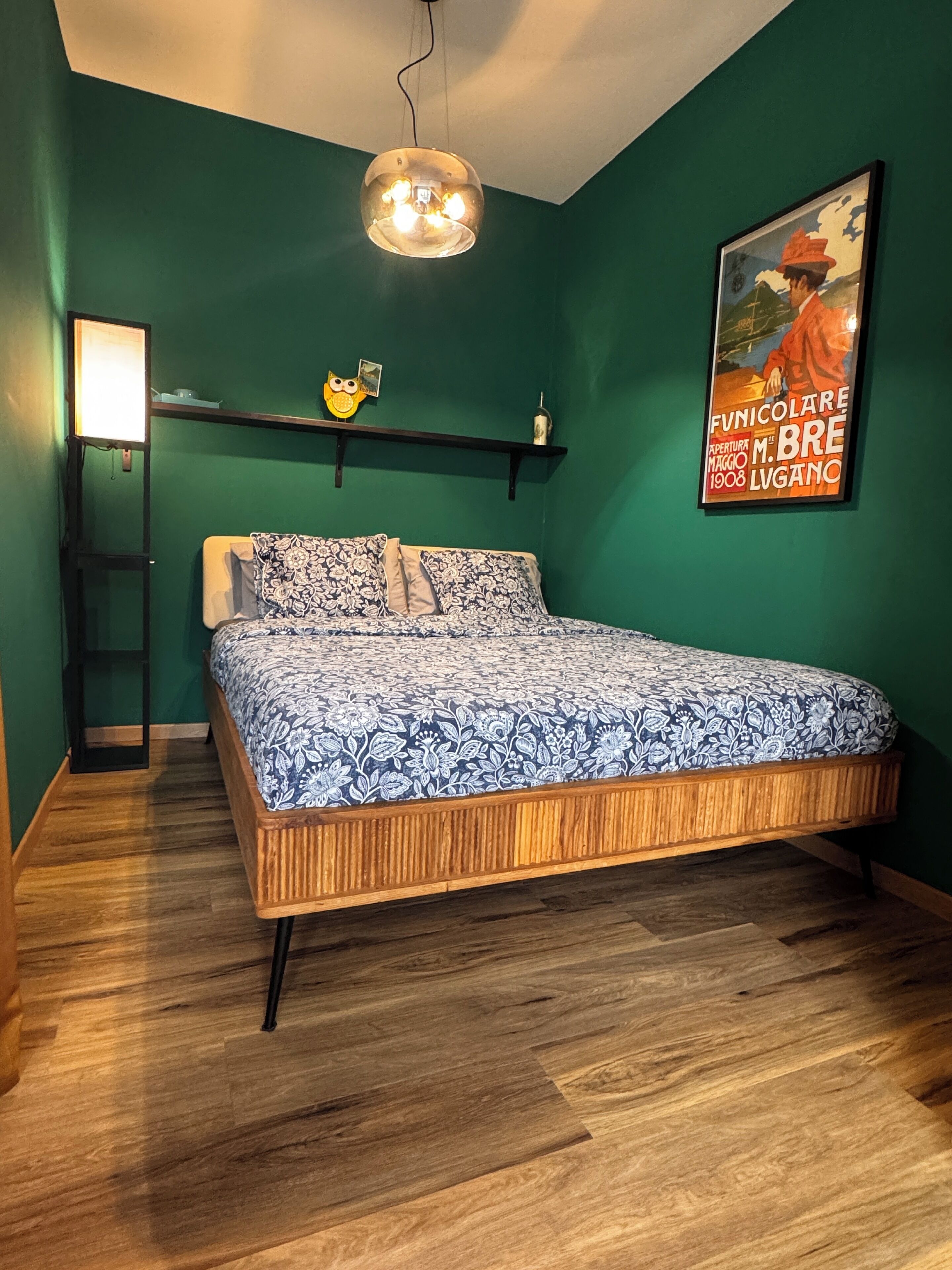 A bedroom with a wooden bed, green walls, a shelf with decorative items, and a poster on the wall.