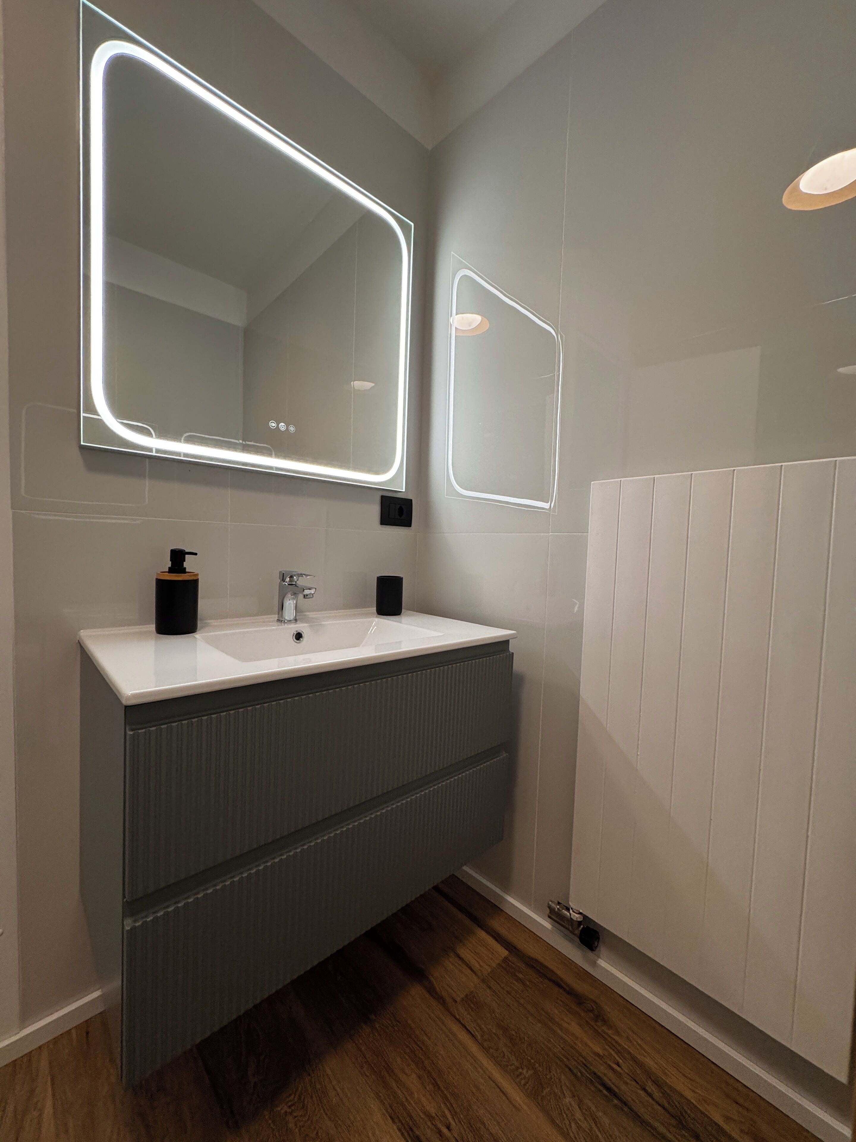 Een moderne badkamer met een grote spiegel, twee wasbakken en een radiator.