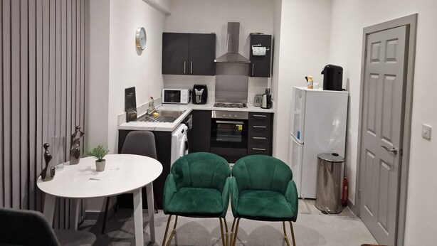 Une cuisine compacte avec un coin repas, comprenant une table blanche, deux chaises vertes et des appareils électroménagers modernes.