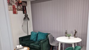 Un salon moderne avec un canapé vert, une petite table ronde et un coin repas comprenant une table blanche et des chaises vertes.