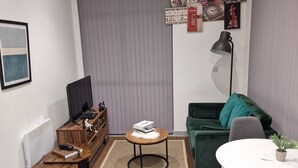 Un salon moderne avec un canapé vert, une petite table ronde, un téléviseur et un panneau indiquant le British Museum.