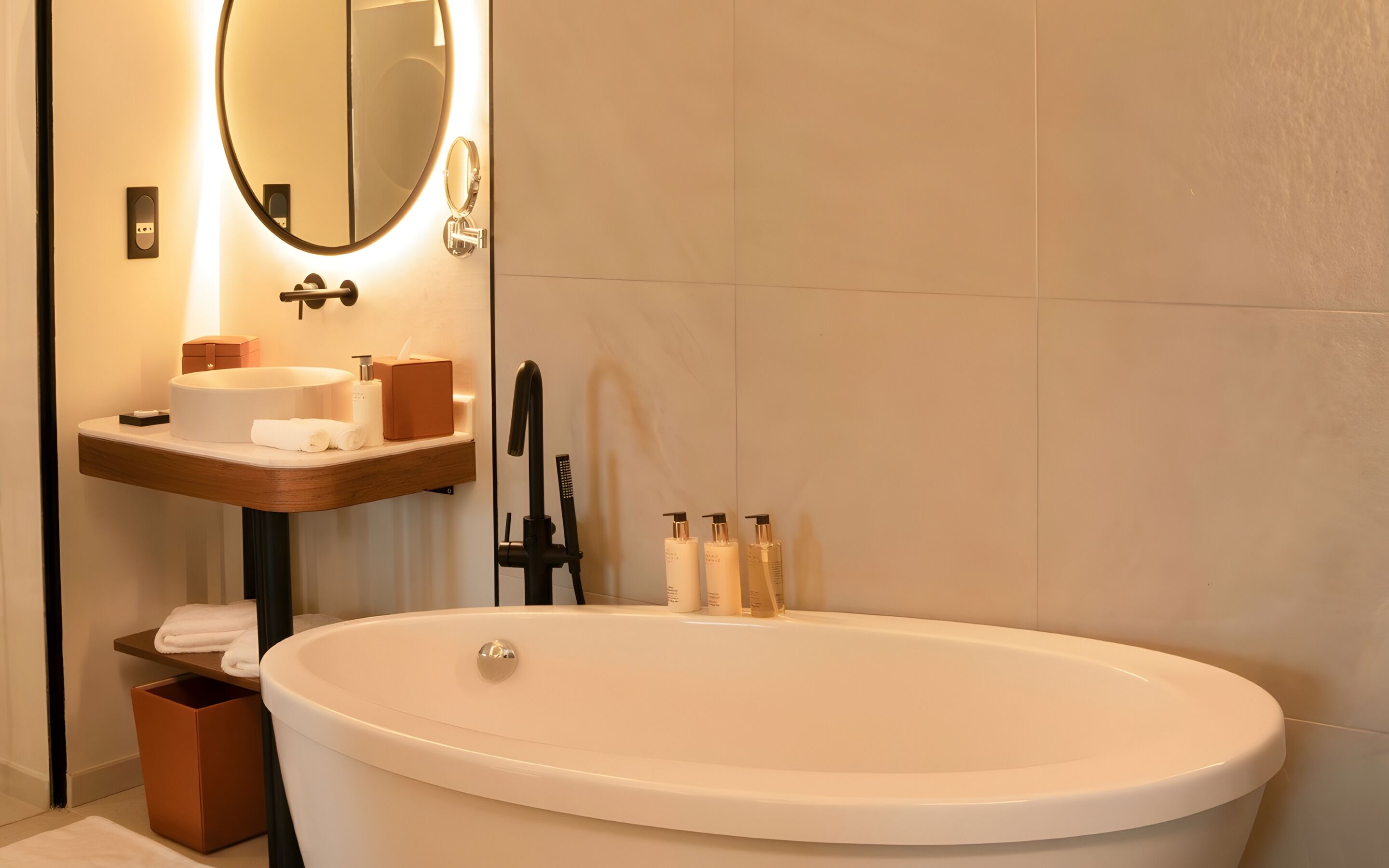 A modern bathroom with a freestanding bathtub, a round mirror, and a wooden vanity with a sink.