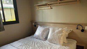 Un lit bien fait, avec une literie et des oreillers blancs, une tête de lit en bois et une fenêtre équipée de stores.