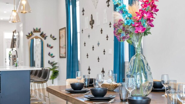 Een eetgedeelte met een houten tafel gedekt voor een maaltijd, een vaas met kleurrijke bloemen, en een moderne keuken op de achtergrond.