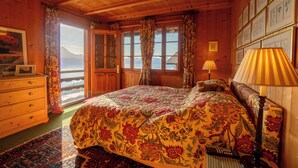 Camera da letto in una baita di legno con un letto grande, una cassettiera e vista sulle montagne.